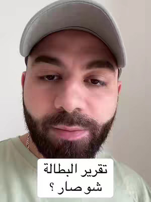 A close-up shot of a man with a beard and a gray cap on his head. He's looking at the camera, and there's text in Arabic at the bottom.