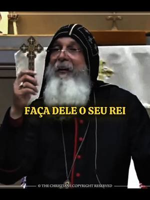 A man in religious attire holds a cross in one hand while gesturing with the other and speaking.