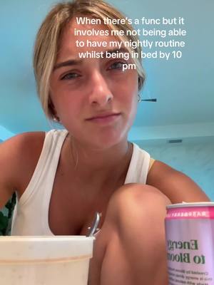 A young woman with blonde highlights poses for a selfie from a low angle. She's wearing a white tank top. Text overlay is present on the top left of the image. In her hands she holds something and a can of a beverage that has the text "bloo" on it. The background is a light blue wall.