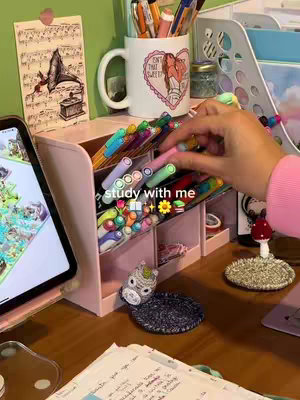 A desk setup with various stationery items, including pens, highlighters, and a tablet, arranged neatly. The scene is brightly lit, suggesting a focus on study or creative work.