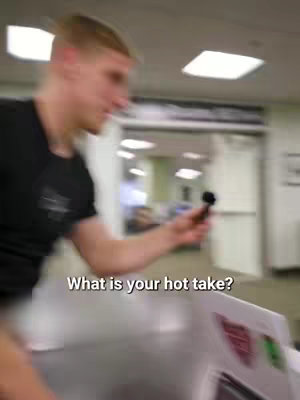 A man in a black shirt holds a microphone while walking in what appears to be a public space. Text overlayed states: "What is your hot take?".