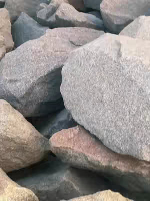 Close-up photograph of several large, irregularly shaped rocks. The rocks vary in color, with shades of gray, tan, and subtle hints of blue and pink. The lighting appears soft and natural, highlighting the textures and uneven surfaces of the stones.