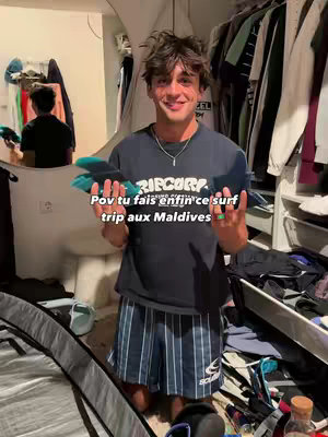 A young man with brown hair and a smile is holding surfboard fins in front of a closet filled with clothes. Text overlays describe the situation.