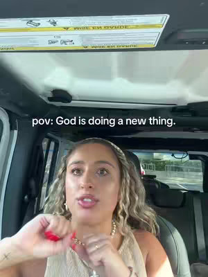 A woman is seated in the driver's seat of a light-colored vehicle, hands on the steering wheel. The image is framed from a POV angle. Above her head, the vehicle’s ceiling and a portion of the windshield are visible.
