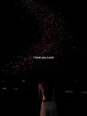 A night scene with a woman facing away from the camera towards a display of lights above. The text 'I love you Lord' is overlaid in white.