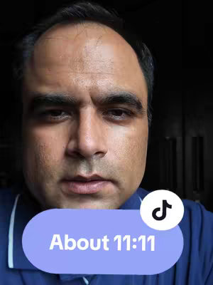 A close-up shot of a man's face, centered, with a light purple oval overlay at the bottom containing the text "About 11:11". The man has short, dark hair and a neutral expression. A TikTok logo is visible within the overlay. The background is dark.