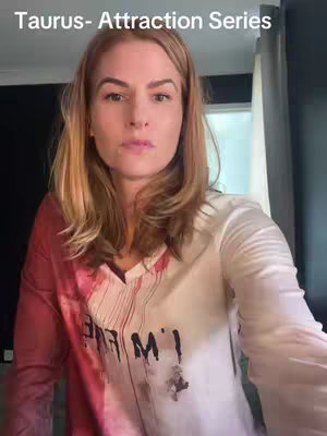 A woman with long blonde hair is in a selfie-style video. She is wearing a white and red shirt. The upper-left of the video has the text reading: 'Taurus- Attraction Series'.
