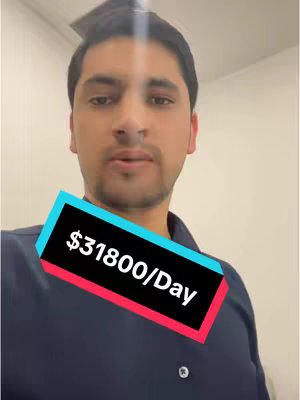 A man in a dark blue golf shirt stands in front of a plain wall with a text overlay. He looks directly at the camera. The text overlay features a black rectangle with the text \"$31800/Day\" in white, positioned horizontally, angled across the bottom of the frame. The man has short, dark hair and a neutral expression.