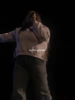 A person singing on a stage with a microphone in hand, dimly lit with text overlayed.