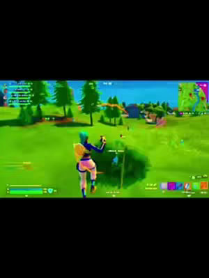 A brightly colored screenshot from the game Fortnite. A character from the game is standing on green grass, facing away from the camera. In the foreground are some green bushes and in the background are trees and buildings with a map overlay in the top right.