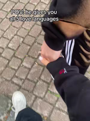 A first-person perspective of two people holding hands while walking on a brick pathway.