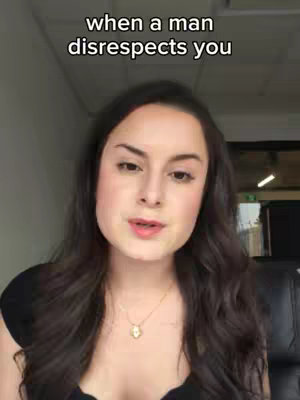 A medium shot of a woman with long, dark hair and a black top, facing the camera slightly. She has a necklace with a pendant. The background shows a blurred office-like setting.