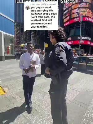A street scene in Times Square featuring two men and a background with large, brightly lit advertisements. The framing is a medium shot, with the men close to the center of the frame. The man on the left wearing a white shirt is holding a small item, while the second man on the right is wearing a police uniform. A comment with text is also presented in the frame.