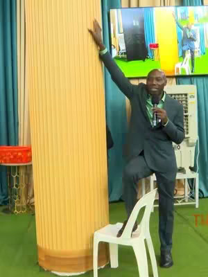 The cover image presents a man speaking in a church setting. He is wearing a dark grey suit with a green shirt, standing next to a large, yellow column. He has one arm raised and is holding a microphone. A television screen in the background is showing an image of the man speaking in a similar setting, along with additional objects such as an air conditioner and chairs. The color scheme appears to primarily consist of shades of green, white, and yellow.