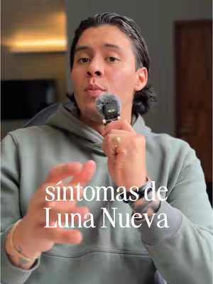 A man with dark hair and a slight beard, wearing a gray hoodie, is holding a small microphone. The background is blurred, suggesting an indoor setting. Text in white overlays the image.