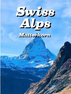 The image captures the Matterhorn mountain, a prominent peak of the Swiss Alps. Above the mountain, the sky transitions from light blue to a bright clear color. In the foreground, the mountain's lower sections and a rugged cliffside are visible, with some snow. The scene highlights the sharp angles and icy slopes of the mountain and the vast blue sky.