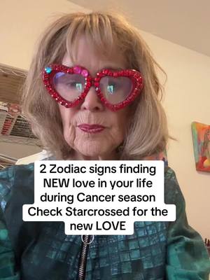 A selfie featuring a woman with heart-shaped bedazzled glasses looking directly at the camera. Text is overlaid on the bottom, and the woman is wearing a colorful jacket. The background is neutral with a glimpse of a shelf and artwork.