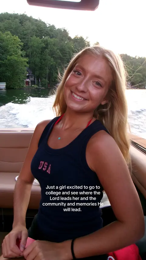 A young woman smiles at the camera while on a boat. Behind her, there is a scenic view of trees and a lake. The text overlay at the image's edges displays text.