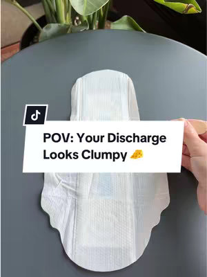 The cover image features a white sanitary pad with an overlay text box bearing the TikTok logo. The pad is resting on a gray surface, positioned in front of a background that includes a partly visible green plant in a pot. A hand is partially visible holding the pad. The video title 'POV: Your Discharge Looks Clumpy' is overlaid as a hook, along with a yellow cheese emoji.