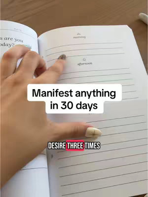 A person's hand, with long nails, pointing at a journal. The open pages include handwriting and lines for writing. The cover image shows text overlays in a white box.