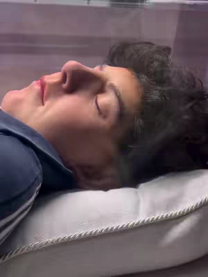 The cover image shows a close-up shot of a person, possibly lying in a bed or on a comfortable surface. The person is seen from the side, with their eyes closed and resting peacefully, suggesting sleep or a moment of relaxation. They are lying on a white pillow, with the rest of the background out of focus. The lighting appears soft, and the overall composition conveys a sense of tranquility, with an object in the background that looks like plastic.