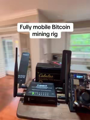 The cover image displays a Bitcoin mining rig setup on a wooden table indoors. A sign on the top of the image mentions: Fully mobile Bitcoin mining rig.