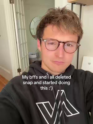 A young man with short brown hair, wearing glasses and a black hoodie with a white design, poses in front of a bright, neutral-toned interior, likely a home. Overlay text indicates he and his friends deleted an app to try something new.