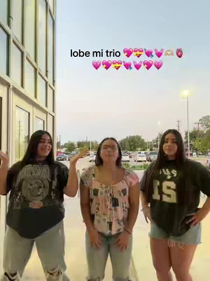 Three young women pose outdoors, against a backdrop of a building with large windows. They are smiling, with the text 'lobe mi trio' and various heart and strawberry emojis above them.