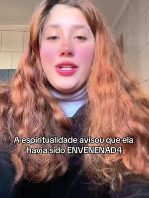A woman with long, reddish-brown hair is centered in the frame, looking directly at the camera. She has rosy cheeks and is wearing a white turtleneck. Above her head, text appears on the image. The background seems to be a neutral interior.