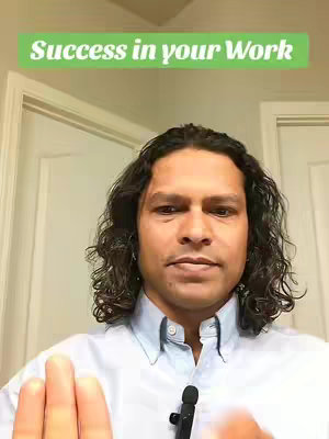 A man with dark hair is centered in the frame, looking at the camera. Above him, a green banner reads 'Success in your Work'. The background consists of a white door and wall, with the man wearing a light blue collared shirt and a microphone clipped to it.
