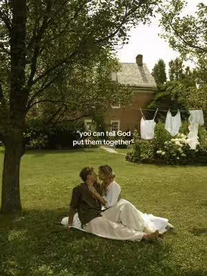 A couple sits embracing on a grassy area, with a blurred tree in the left corner, a house in the background, and laundry hanging on a clothesline to the right. The foreground is focused on the couple with a text overlay.