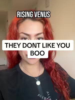 A woman with long, red hair is centered in the frame. Text overlays appear above and below her. She has light skin and is wearing a black shirt with a pendant necklace. The background is a neutral color.