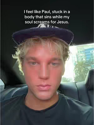 A man with blonde hair and a navy blue hat is seated in a car. The man has his face red, suggesting the use of a filter; he looks contemplative.