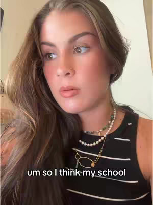 A woman with long brown hair and fair skin looks to her left with a thoughtful expression. She wears a black and white striped tank top and multiple necklaces with a gold pendant. Text overlayed on the bottom reads, "um so I think my school". The background is neutral and softly lit.