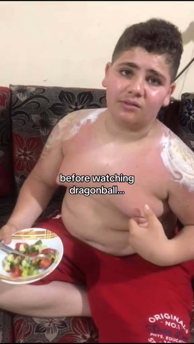 A young, light-skinned male with curly dark hair and a slightly distressed expression sits on a floral-patterned couch. He is wearing red shorts and has what appears to be sunburn on his chest and arms. The text "before watching dragonball..." is overlaid on the image. In his left hand, he holds a plate with a small salad. The overall tone suggests a humorous, relatable situation, possibly about getting ready to watch anime.