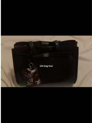 A black bag with a key chain is displayed against a cream-colored background. The bag is a tote bag with two handles and a silver clasp. The keychain has a white and brown pendant with an attached ring that's attached to a bag. The text overlay on image reads, "Uni bag tour".