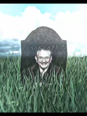 The image shows a gravestone in a field of green grass under a partially cloudy blue sky. The gravestone is engraved with the name "Frank Caprio" and a portrait of the man is presented below his name. He's wearing glasses and a suit and tie, and a smile is visible.