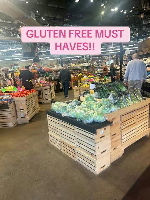 A grocery store scene with a large display of produce in the foreground. The main focus is on the produce section of the store, filled with various fruits and vegetables and a pink overlay that contains text.