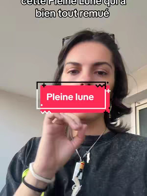 A person with dark hair is centered in the frame, making an 'okay' hand gesture. The person is wearing a black t-shirt and a silver necklace, and there is a bracelet on their left wrist. Overlaid on the image is a graphic with the words 'Pleine lune'.
