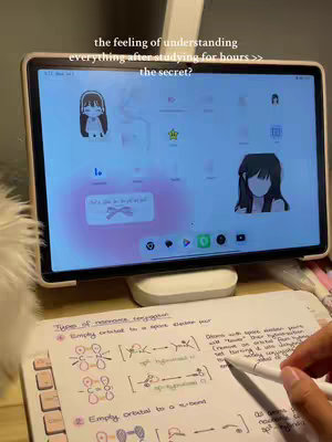 The image shows a tablet propped up on a desk, displaying a screen with cartoon characters. Below the tablet, a page of handwritten notes is visible, with a hand holding a pen. The overall scene suggests a study environment with a focus on learning or note-taking.
