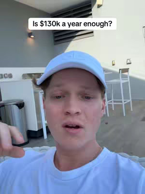 A selfie-style video with a young man in a white cap and t-shirt, posing with a slightly concerned expression, set against a blurred outdoor background.