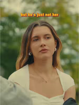 A woman gazes pensively at the viewer, with a text overlay across the top. She has light brown hair and is wearing a white top and hoop earrings, set against a blurred outdoor backdrop.