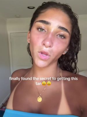 A woman with dark hair and tanned skin is centered in the frame, wearing a blue top. The image emphasizes her face, with a clear contrast between her facial tan and a lighter area around the eyes and mouth. Text overlays add to the overall composition.
