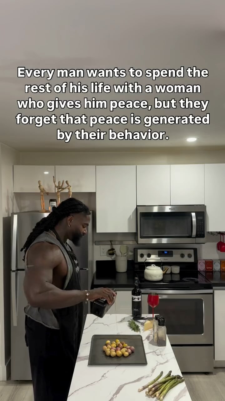 A man with dreadlocks in a gray vest and black apron is in a kitchen, pouring from a dark bottle into a bowl of grapes as the text overlay sits above him. The kitchen has white cabinets, stainless steel appliances, and a white countertop. The man is muscular and is in the middle of a kitchen setting with a black surface countertop with food and drink for the camera shot.