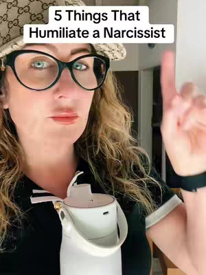 A woman with light skin and curly hair is the focal point of the image, set against a blurred interior background. She is wearing a black top with a white trim or collar and large black-rimmed glasses. Her expression is not fully visible, but she has a slight smirk, and she points her index finger up.