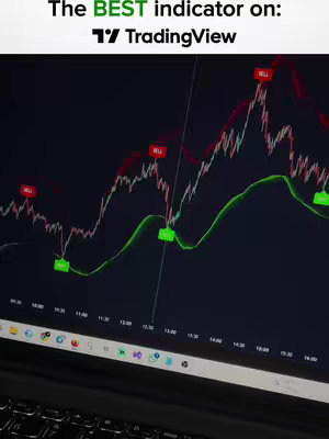 Image shows a laptop screen displaying a technical analysis chart. The chart features red and green lines indicating price movements, with green indicators labeled “BUY” and red indicators labeled “SELL” overlayed in the video. The background is dark, and the image has a slight angle.