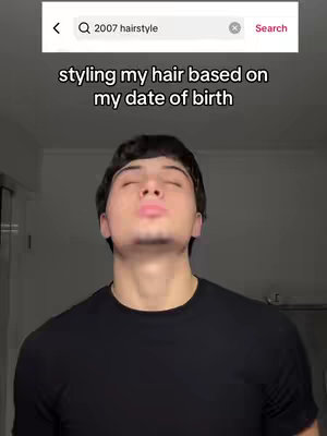 A young man in a black shirt is the central figure, looking upwards with his eyes closed and mouth slightly open, as if in a pose. The background is a plain, light-colored wall. Overlayed, there is a search bar displaying the text '2007 hairstyle' with a search icon along with the text 'Styling my hair based on my date of birth'.