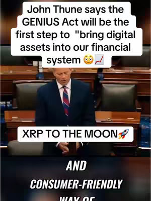 A video cover featuring a man speaking at a podium with text overlays promoting cryptocurrency. The man is wearing a dark suit and tie, positioned in what appears to be a legislative chamber. Text overlays include "John Thune says the GENIUS Act will be the first step to"bring digital assets into our financial system", "XRP TO THE MOON" , and "AND CONSUMER-FRIENDLY WAY OF". The background shows wooden paneling and seating.