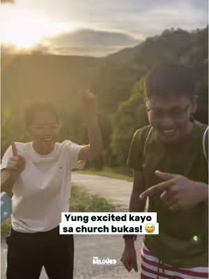 Two young men are captured in a sunlit outdoor setting, likely a park or open area with rolling hills in the background. The man on the left is wearing a plain white t-shirt, black pants, and his right arm is raised upwards, as if celebrating. He's smiling and pointing towards the camera. The man on the right, wearing a green top and striped shorts, is also smiling and pointing. A text overlay in a yellow box at the bottom of the image reads, "Yung excited kayo sa church bukas!" with a smiling face emoji, suggesting excitement about attending church the next day.