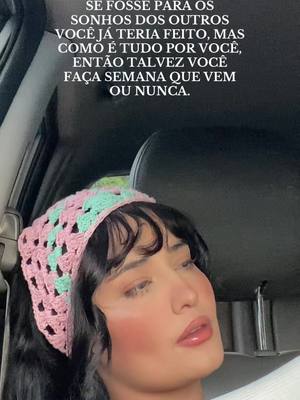 A woman in a car wearing a crochet headband looks off to the side with a contemplative expression. The background shows the car's interior.